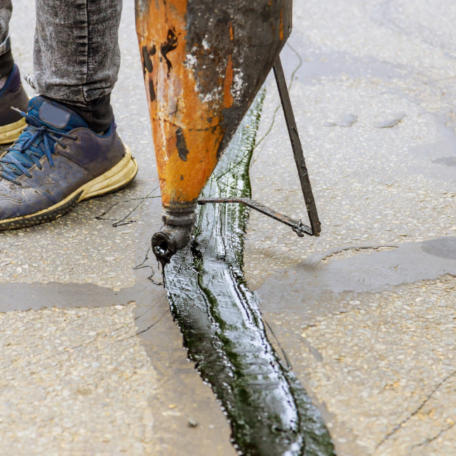 worker filling a crack on the floor with an asphalt machine